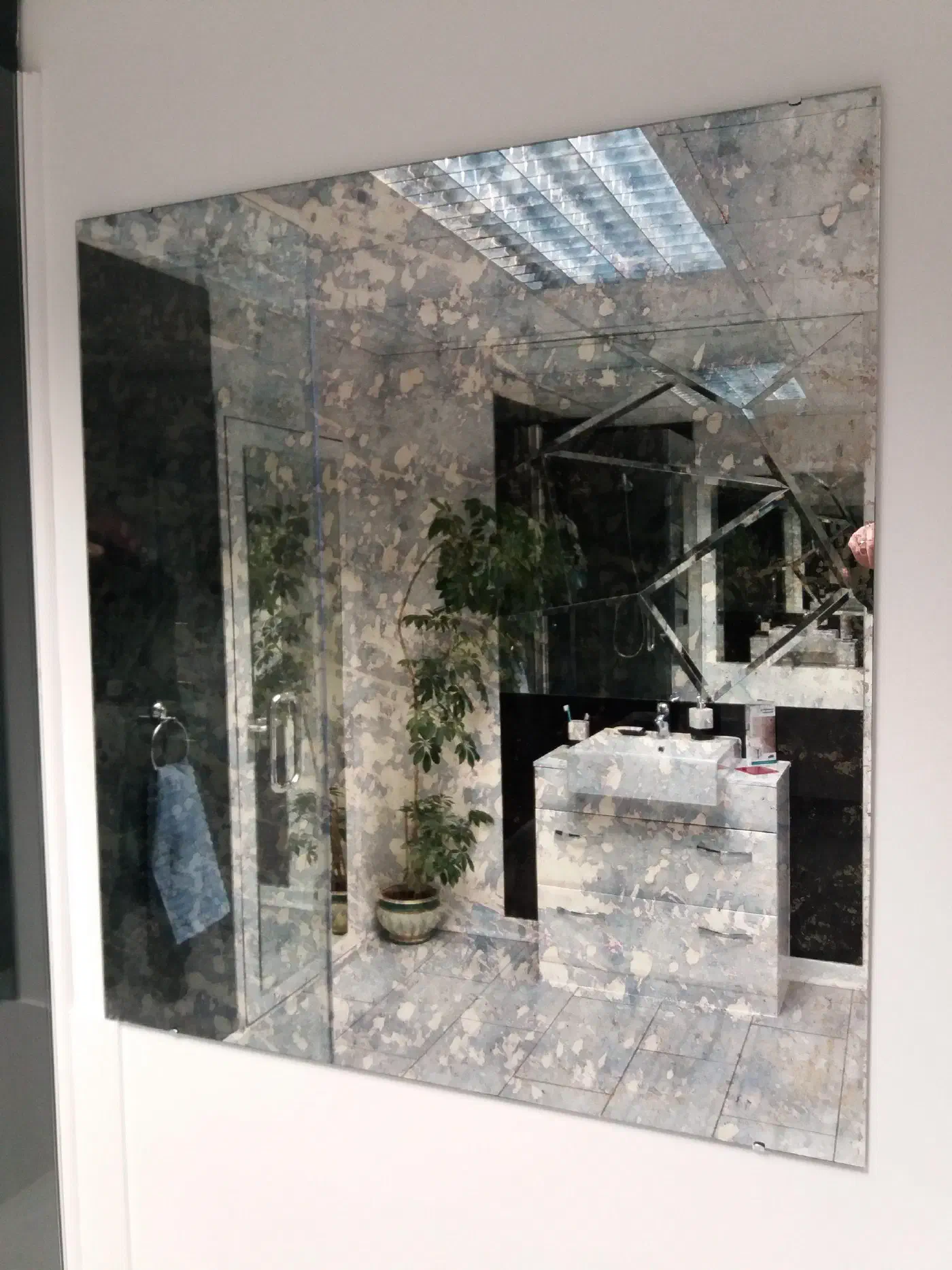 A wall-mounted antique mirror with a mottled, aged finish and bevelled panels, reflecting a bathroom