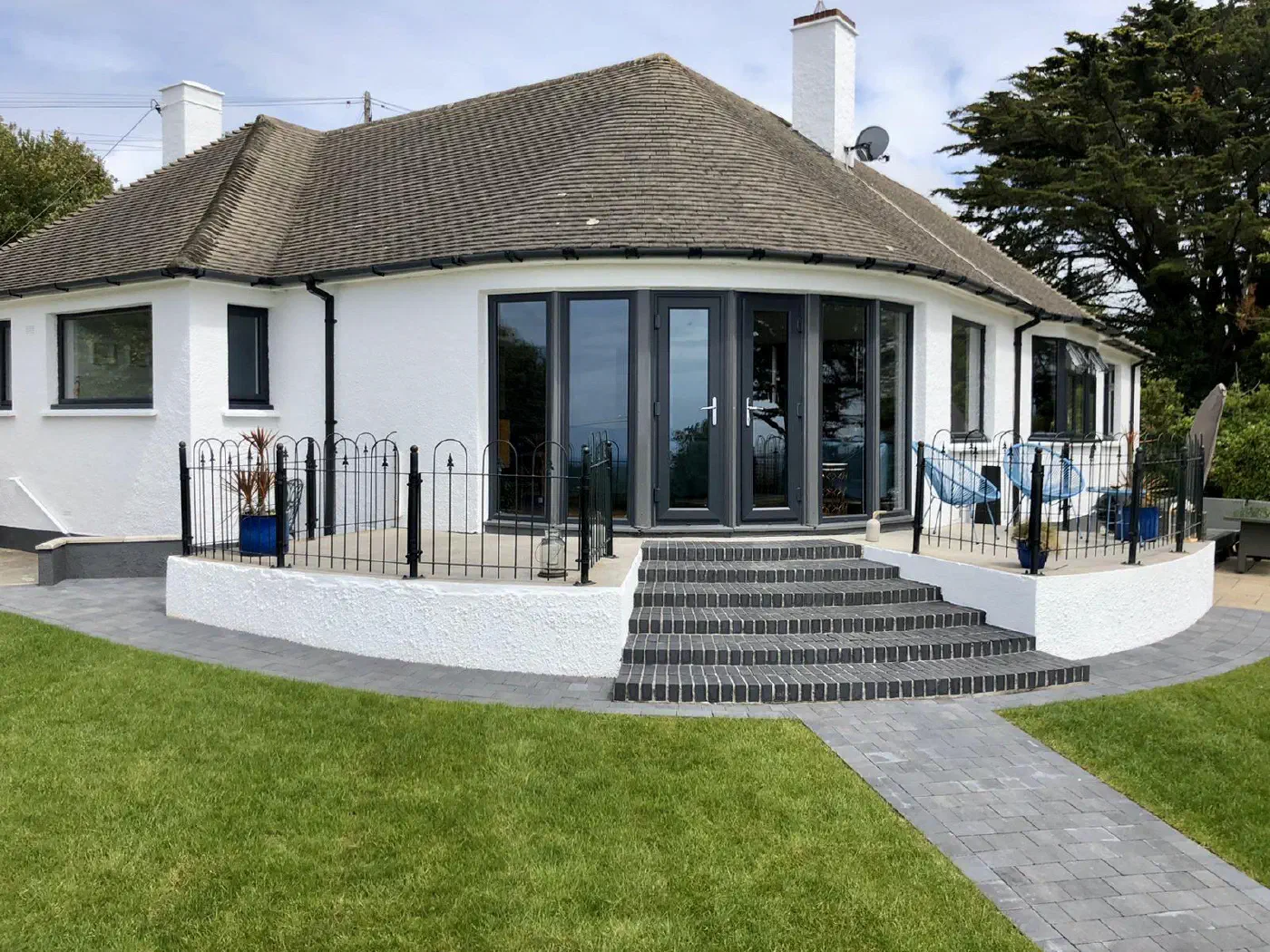 The rear of a white rendered bungalow with new dark grey French doors and windows opening onto a raised terrace