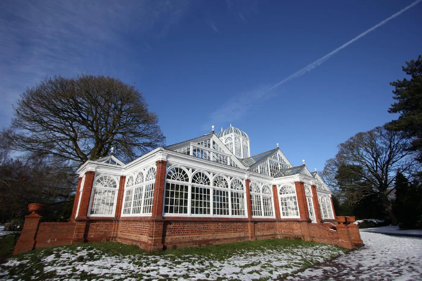 A white-framed Victorian conservatory with a domed lantern roof, on a red-brick base, in winter light