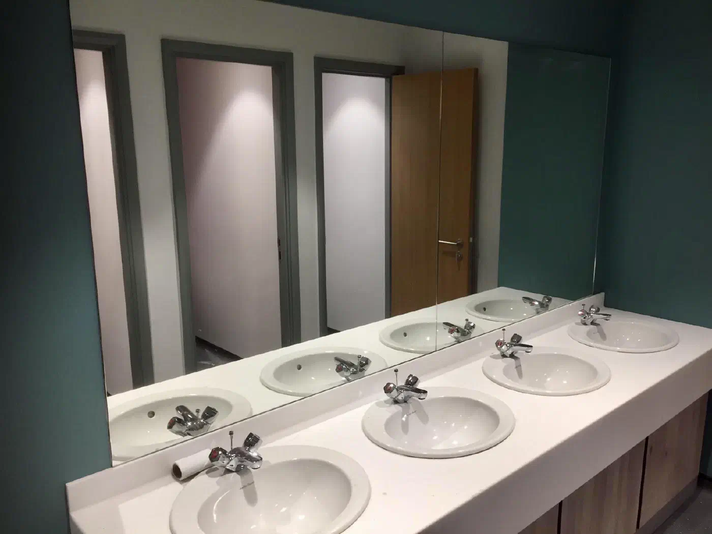 A full-width mirror above a row of four washroom basins